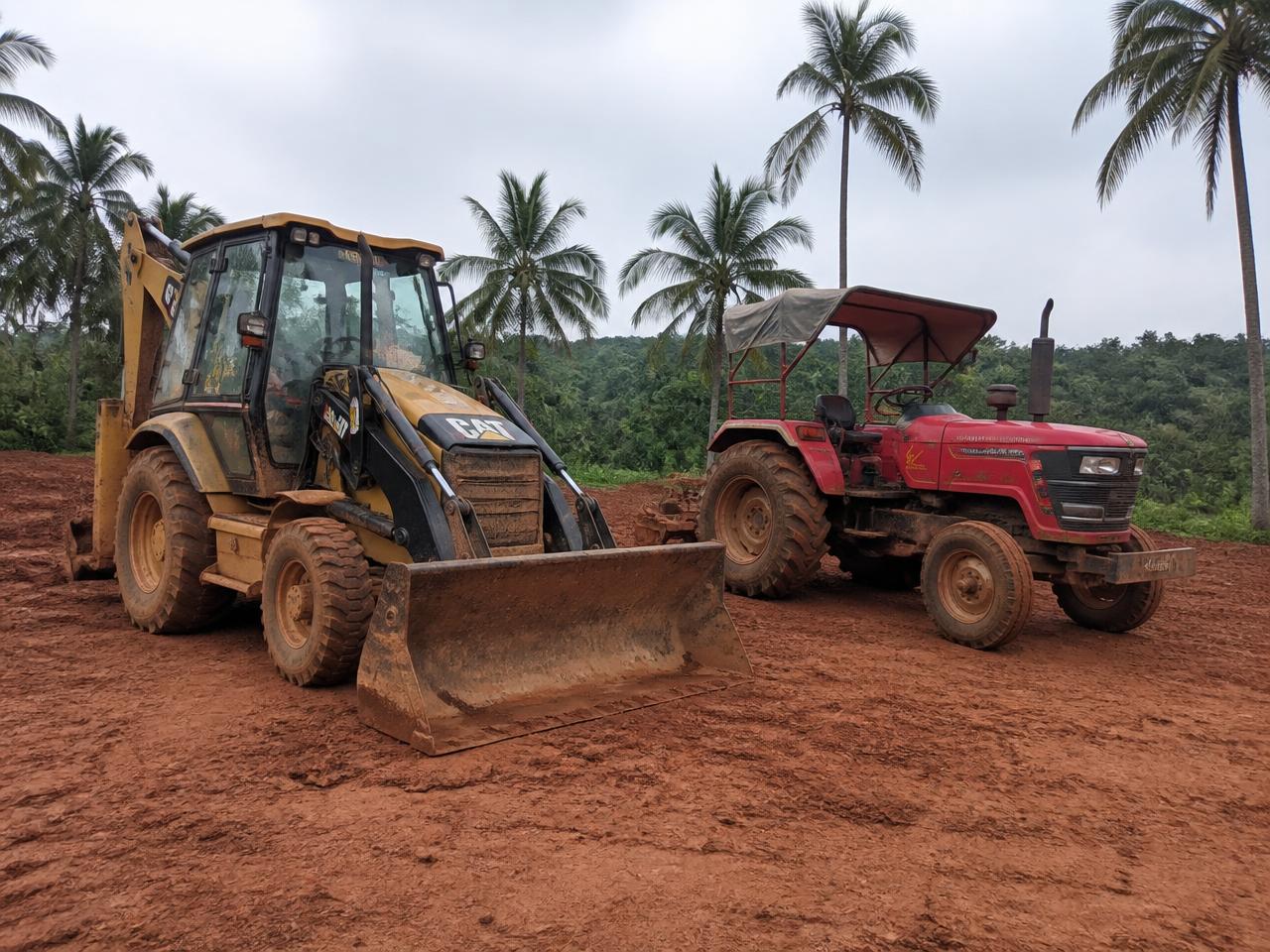 A backhoe loader and farm tractor parked on a rural Jamaican work site